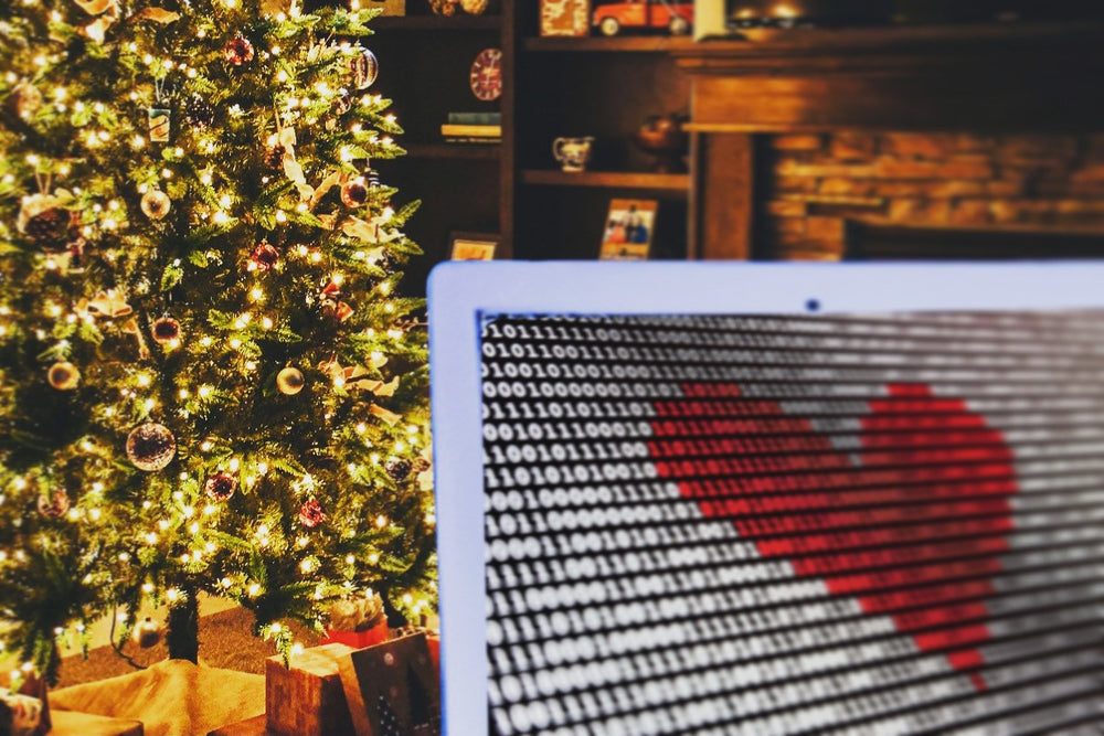 This image was suggest by ChatGPT by OpenAI, an artificial intelligence language model. It depicts a computer screen showing off binary code in front of an artificial christmas tree lit with warm white lights for the holiday season.