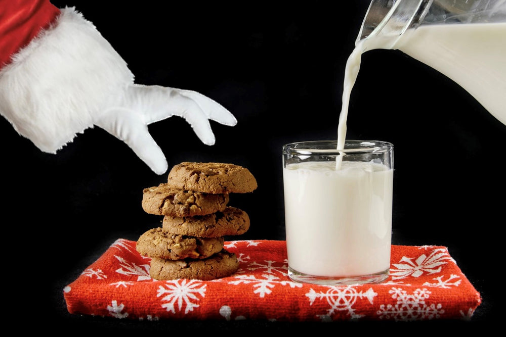 Santa Claus reaching for a chocolate chip cookie next to a glass of fresh milk
