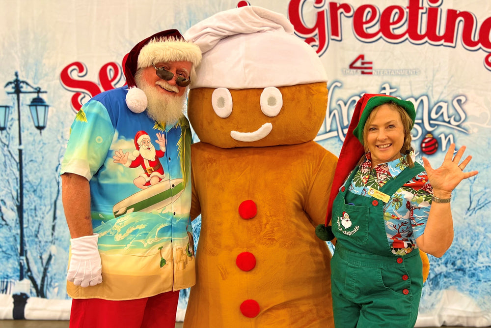 Santa Claus, in a beach-ready summer outfit, posing with GB Spice and a Rent-A-Christmas Elf at Christmas Con CA 2022 in Pasadena, California.